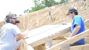 JONATHAN ROWE | DAILY NEWS ROOFING: Cameron Jennings, Bryan Raehl and Matias Palmisano measure and discuss plans to add to the roof of Louise Hill’s new home. The volunteer laborers will be working at the site all week. 