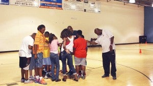 CAROLINE HUDSON | DAILY NEWS BOW IN: Phil Ford joins the basketball campers at Fitness Unlimited and coach John Lampkins in a prayer to close out the events of Monday’s camp group. Ford said his faith has played a large role in his life. 